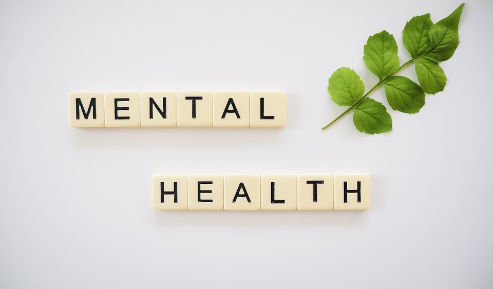 Mental health letter tiles arranged beside green leaves